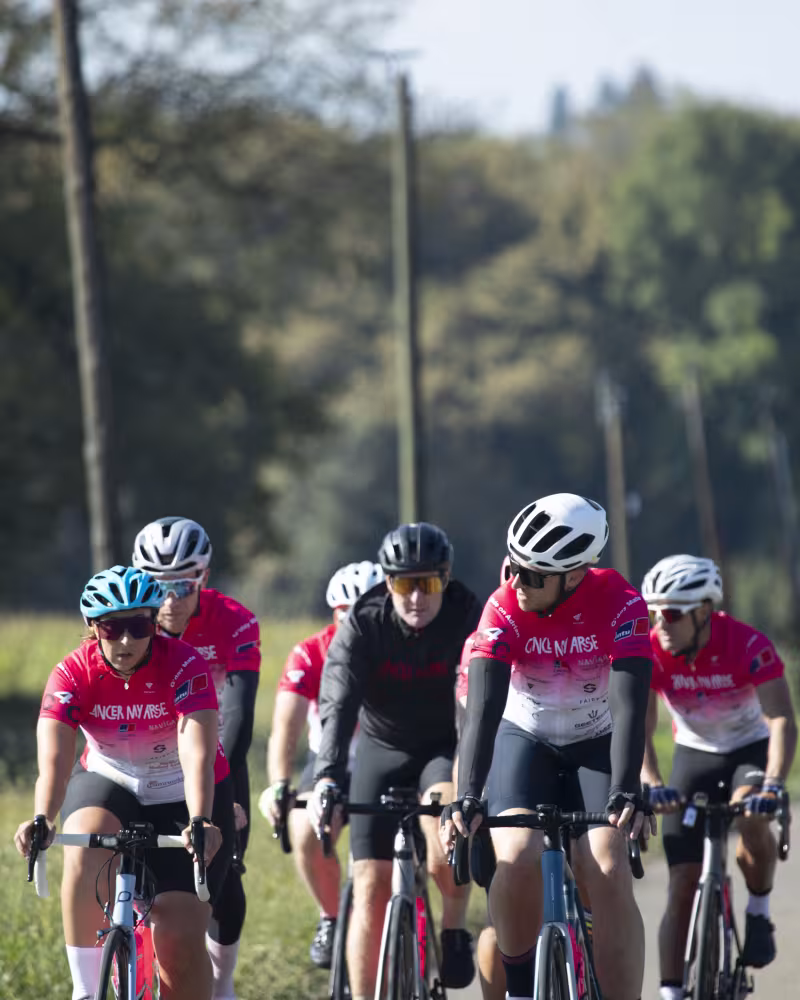 A group of riders in pink Cancer My Arse kit cycling along a tree-lined country road
